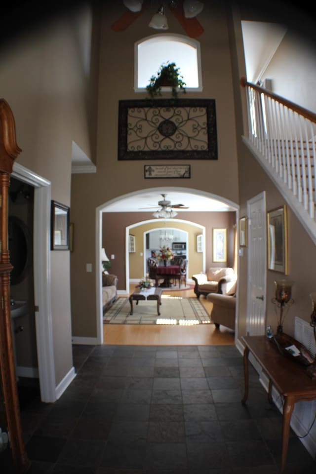 entryway with arched walkways, baseboards, ceiling fan, and a towering ceiling