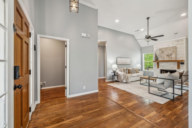 living area featuring wood finished floors, high vaulted ceiling, baseboards, ceiling fan, and a large fireplace