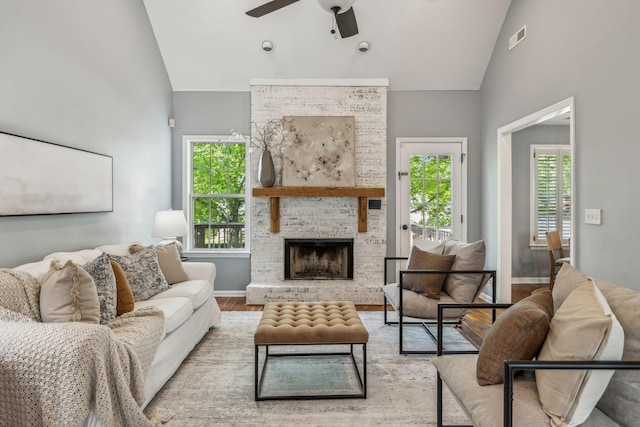 living area with wood finished floors, a ceiling fan, high vaulted ceiling, a brick fireplace, and visible vents