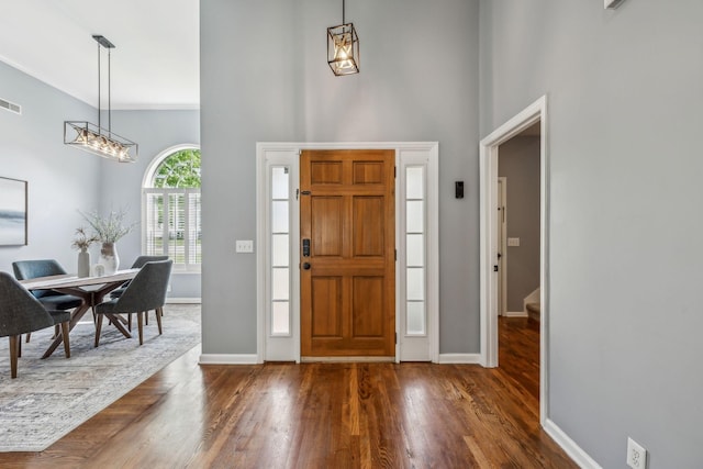 entrance foyer with visible vents, dark wood finished floors, a chandelier, a high ceiling, and baseboards