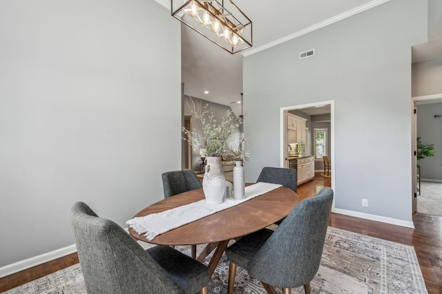 dining space with wood finished floors, crown molding, visible vents, baseboards, and a chandelier