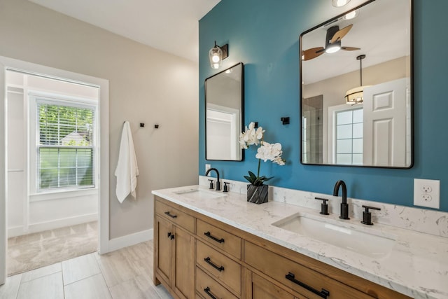 full bath featuring baseboards, a shower, double vanity, and a sink