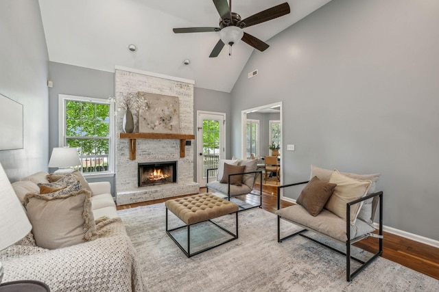 living area featuring wood finished floors, high vaulted ceiling, visible vents, a large fireplace, and baseboards
