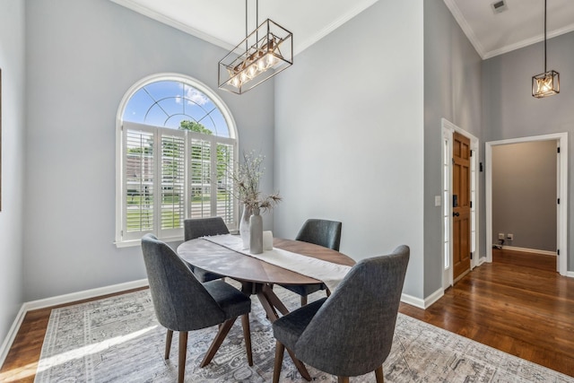 dining space with baseboards, ornamental molding, an inviting chandelier, wood finished floors, and a high ceiling