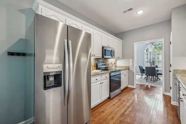 kitchen featuring wood finished floors, stainless steel appliances, white cabinetry, visible vents, and backsplash