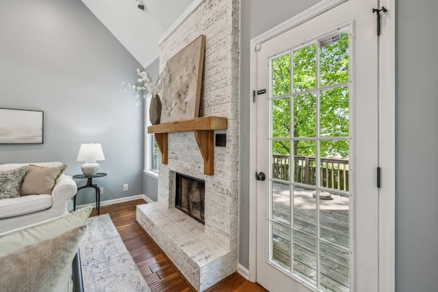 living area featuring plenty of natural light, vaulted ceiling, a brick fireplace, and dark wood-type flooring