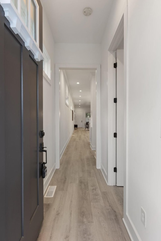 hallway with baseboards, visible vents, and light wood-type flooring