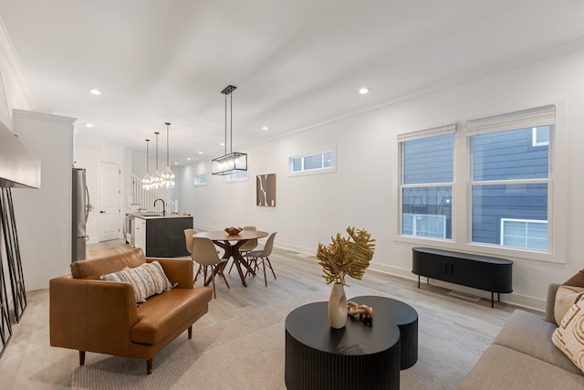 living area featuring light wood-type flooring, baseboards, recessed lighting, crown molding, and a notable chandelier