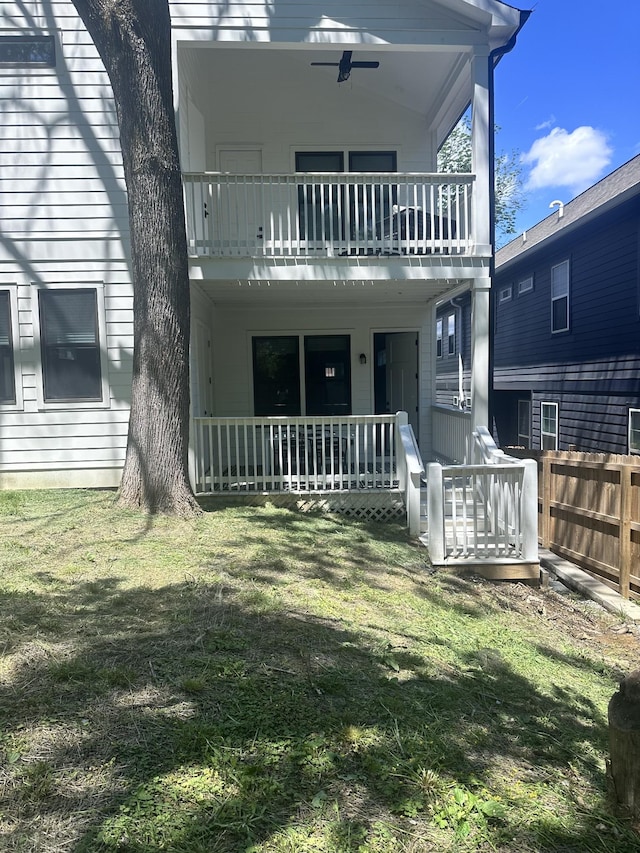 rear view of house featuring a balcony, covered porch, fence, and a lawn