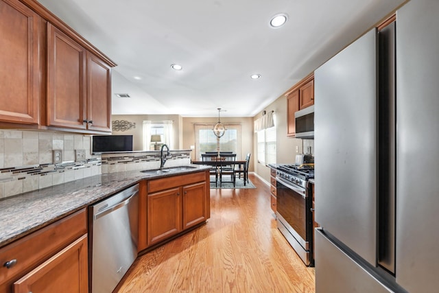 kitchen with light wood-type flooring, stainless steel appliances, brown cabinetry, and a sink