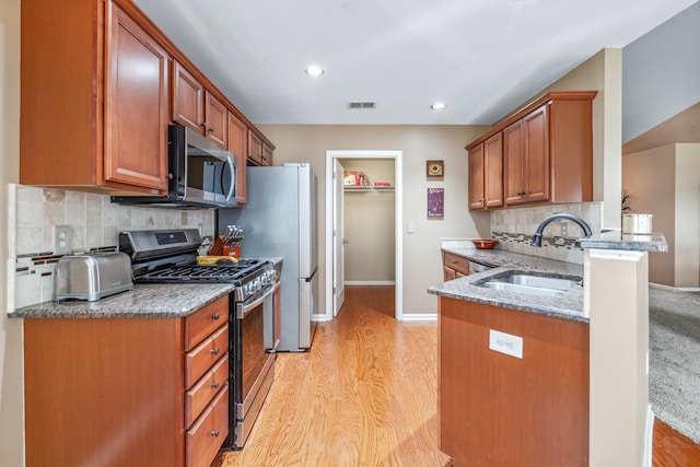 kitchen with a sink, visible vents, light wood-style flooring, backsplash, and appliances with stainless steel finishes