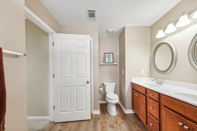 bathroom featuring a sink, toilet, wood finished floors, visible vents, and double vanity