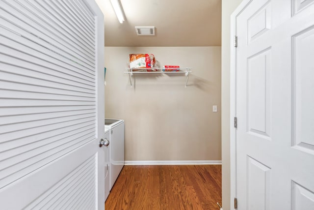 clothes washing area with wood finished floors, laundry area, visible vents, washing machine and clothes dryer, and baseboards