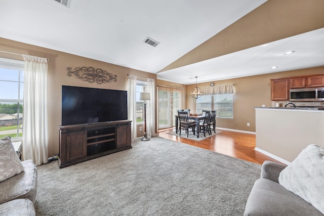 living area with lofted ceiling, light colored carpet, baseboards, visible vents, and a notable chandelier