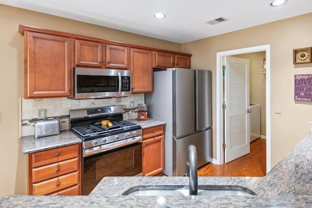 kitchen featuring wood finished floors, a sink, stainless steel appliances, visible vents, and tasteful backsplash