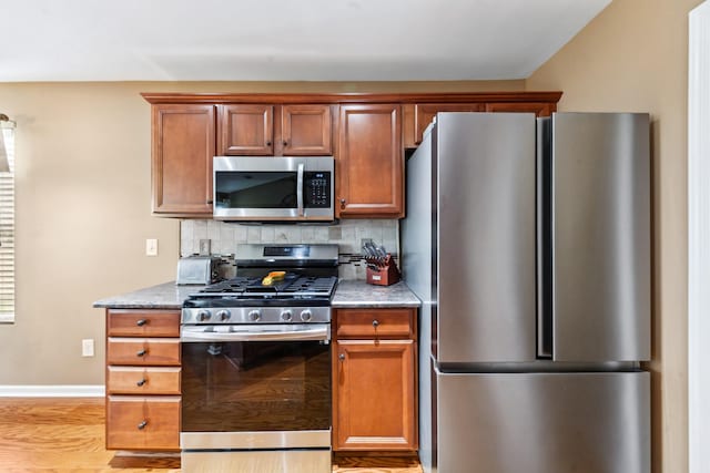 kitchen with brown cabinetry, light wood finished floors, decorative backsplash, baseboards, and appliances with stainless steel finishes