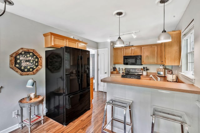 kitchen featuring a peninsula, light countertops, light wood-style floors, and black appliances