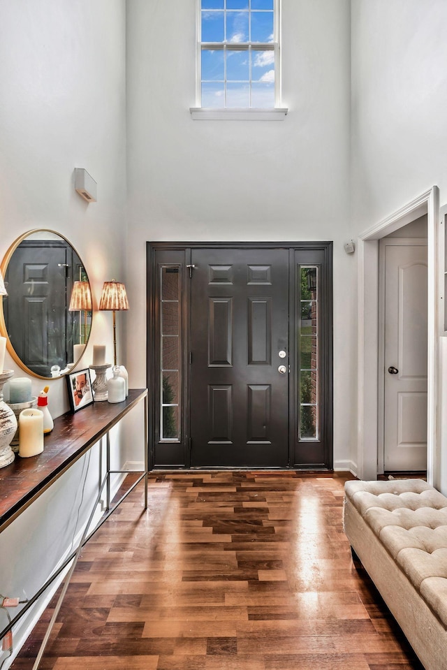 entryway featuring baseboards, a towering ceiling, and wood finished floors