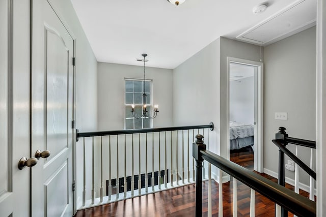 hall with a notable chandelier, attic access, baseboards, wood finished floors, and an upstairs landing
