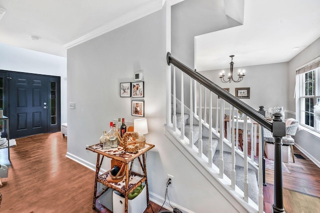 stairs with baseboards, an inviting chandelier, crown molding, and wood finished floors