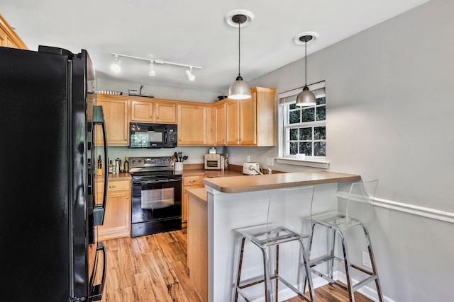 kitchen with light brown cabinetry, a kitchen bar, a peninsula, black appliances, and light wood-type flooring
