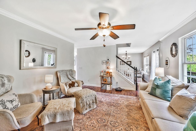 living area featuring stairs, ceiling fan with notable chandelier, wood finished floors, ornamental molding, and baseboards