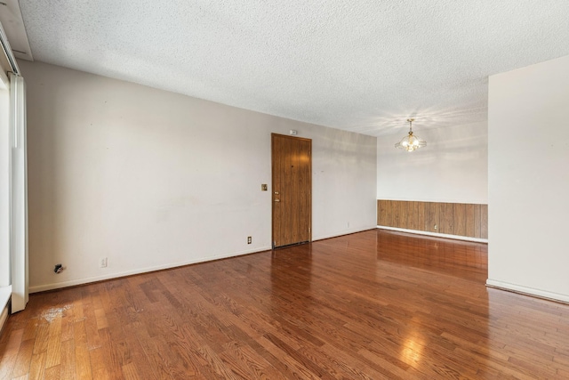 empty room with an inviting chandelier, a textured ceiling, wood finished floors, and a wainscoted wall