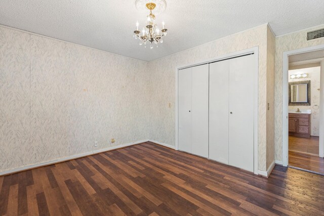 unfurnished bedroom with wood finished floors, wallpapered walls, a notable chandelier, a textured ceiling, and visible vents