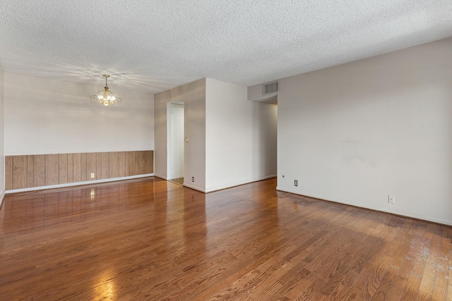 empty room with an inviting chandelier, a textured ceiling, visible vents, and wood finished floors