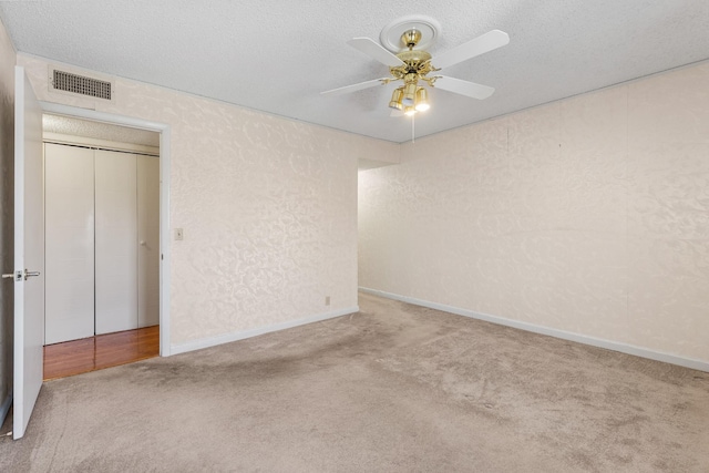 carpeted empty room featuring a textured ceiling, visible vents, ceiling fan, and a textured wall
