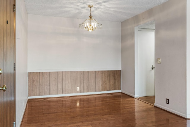 spare room with a textured ceiling, baseboards, wood walls, a chandelier, and wood finished floors