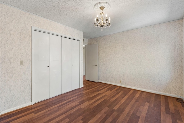 unfurnished bedroom with a notable chandelier, a closet, wallpapered walls, a textured ceiling, and wood finished floors