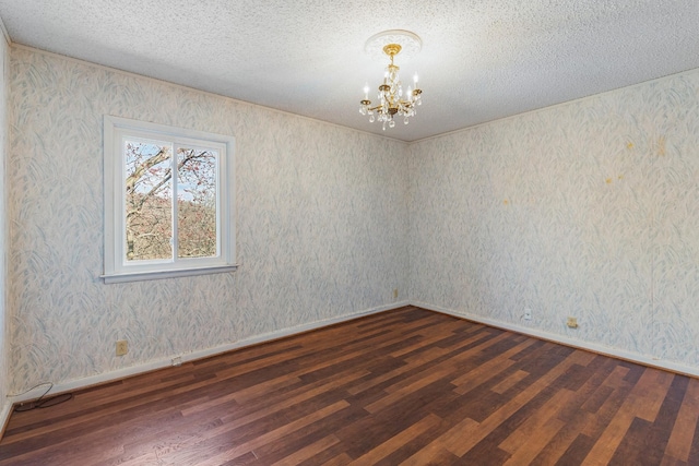 empty room with a notable chandelier, wallpapered walls, a textured ceiling, and wood finished floors