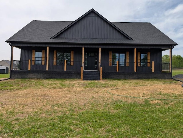 view of front facade with a porch, roof with shingles, a front lawn, and board and batten siding