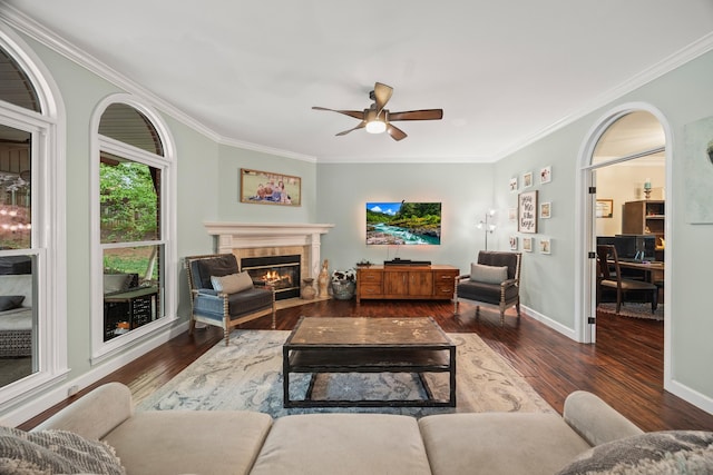 living area with ceiling fan, a tiled fireplace, crown molding, and wood finished floors