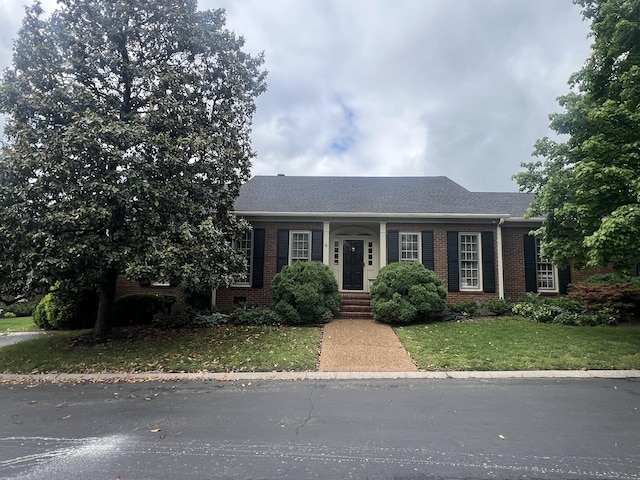 ranch-style home with a shingled roof, brick siding, and a front lawn