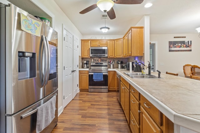 kitchen featuring a peninsula, a sink, dark wood finished floors, light countertops, and appliances with stainless steel finishes