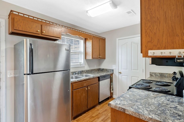 kitchen with appliances with stainless steel finishes, light wood-style flooring, brown cabinets, and a sink