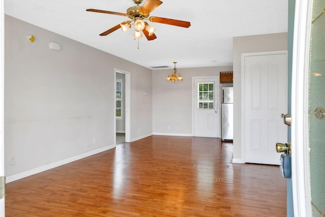 empty room featuring light wood finished floors, visible vents, baseboards, and ceiling fan with notable chandelier