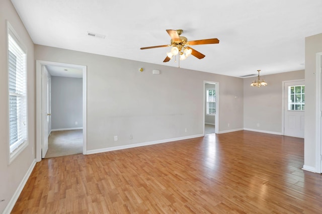empty room featuring plenty of natural light, visible vents, light wood-style flooring, and ceiling fan with notable chandelier