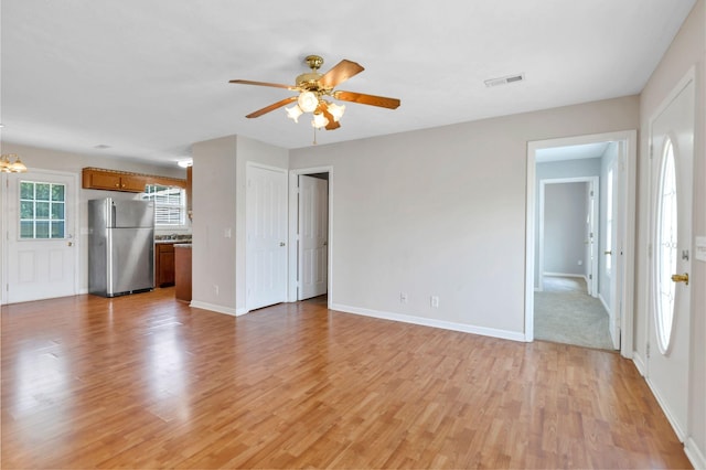 unfurnished living room with light wood finished floors, ceiling fan with notable chandelier, baseboards, and visible vents