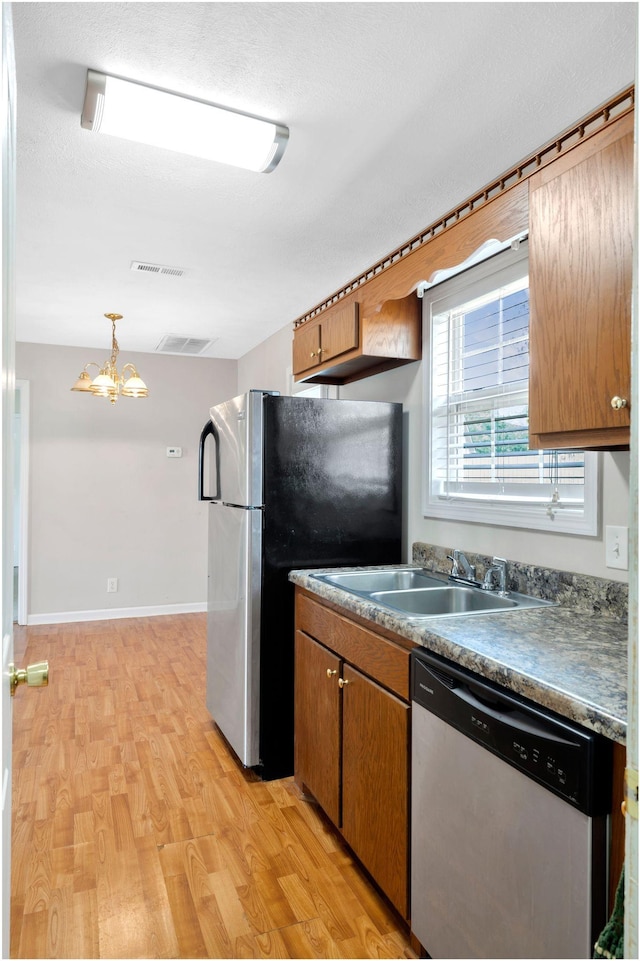 kitchen with appliances with stainless steel finishes, an inviting chandelier, visible vents, a sink, and light wood-type flooring