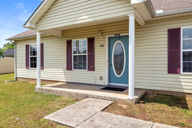 entrance to property featuring a yard, roof with shingles, and fence