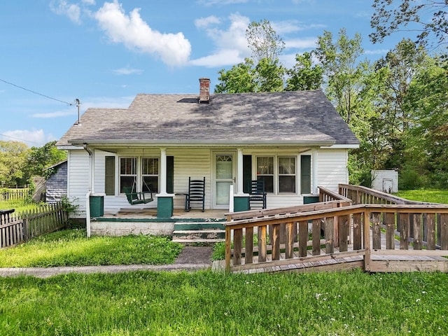 rear view of house with a chimney, roof with shingles, covered porch, and fence