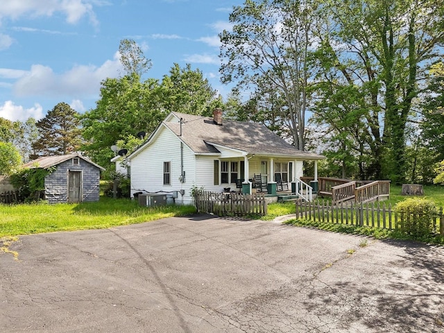view of front of house featuring a chimney, an outbuilding, a shed, a fenced front yard, and a porch