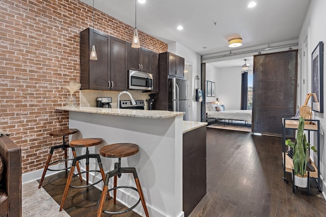 kitchen featuring a breakfast bar area, stainless steel appliances, dark brown cabinetry, dark wood finished floors, and light stone countertops