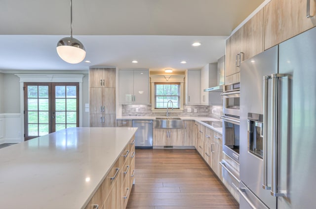 kitchen featuring light brown cabinetry, light stone countertops, modern cabinets, a sink, and stainless steel appliances