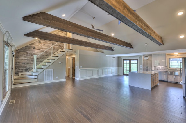 unfurnished living room featuring a ceiling fan, wainscoting, visible vents, stairs, and vaulted ceiling with beams