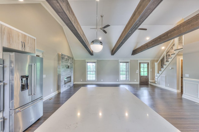 unfurnished living room with beamed ceiling, dark wood-type flooring, a ceiling fan, and a stone fireplace
