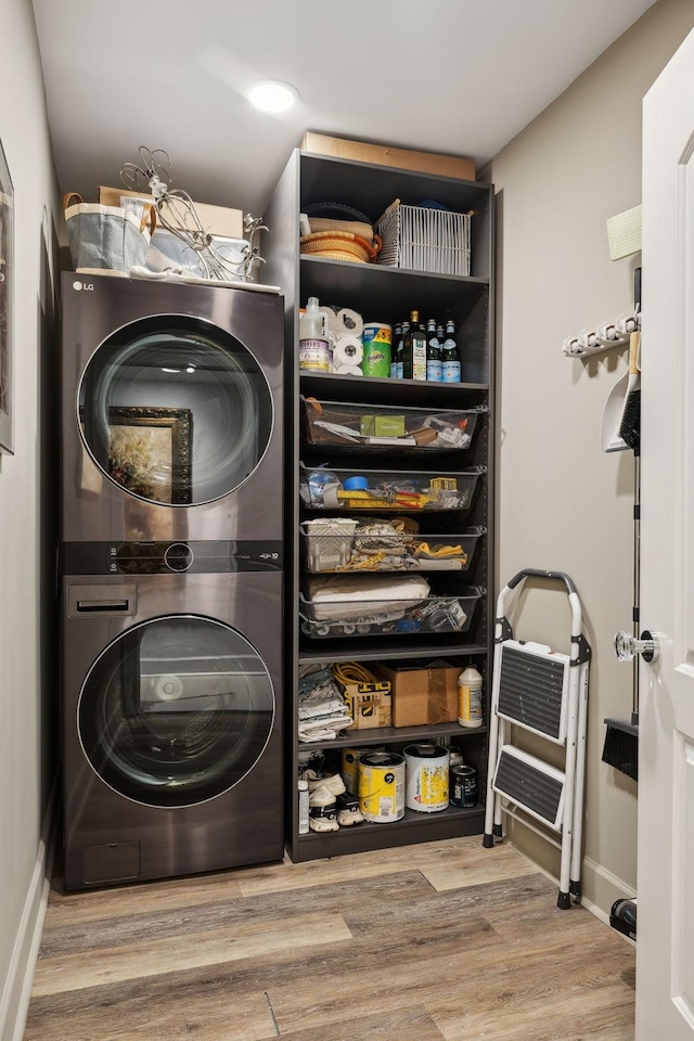 clothes washing area featuring laundry area, stacked washer / dryer, wood finished floors, and baseboards